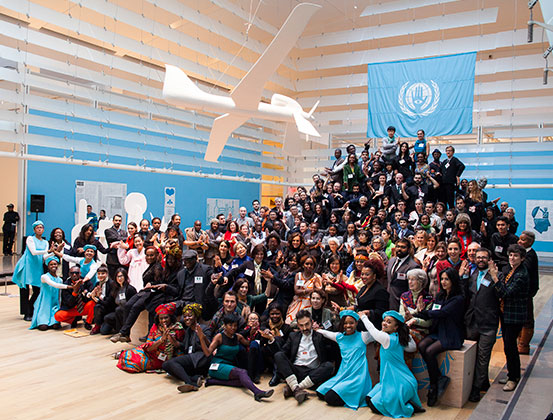 Citizen-delegates and other participants of The People’s United Nations (pUN), Drone Dove in foreground and official pUN flag with motto “Hands-on with a vision” in background. Queens Museum, New York City, 2013. Courtesy of the artist.