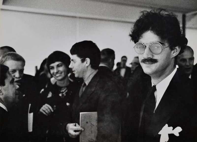 Julian Wasser. "Larry Bell at the Opening Reception (Ed Moses and Robert Irwin in background), Duchamp Retrospective, Pasadena Art Museum, 1963." Vintage gelatin silver print. 9.5 x 13.5”. Courtesy Robert Berman/E6 Gallery
