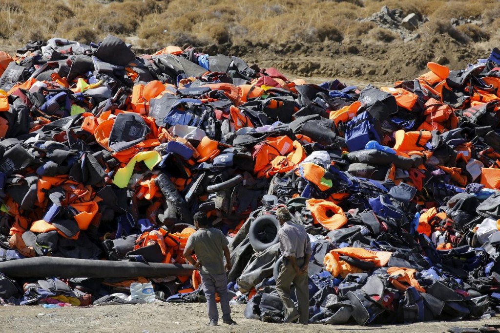 Locals survey a huge pile of deflated dinghies, tubes and life vests left by arriving refugees and migrants on the Greek island of Lesbos on Sept. 18, 2015. Photograph by Yannis Behrakis/Reuters.